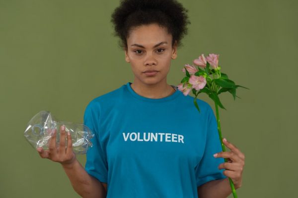 Portrait of a volunteer promoting environmental conservation, holding recycled plastic and flowers.